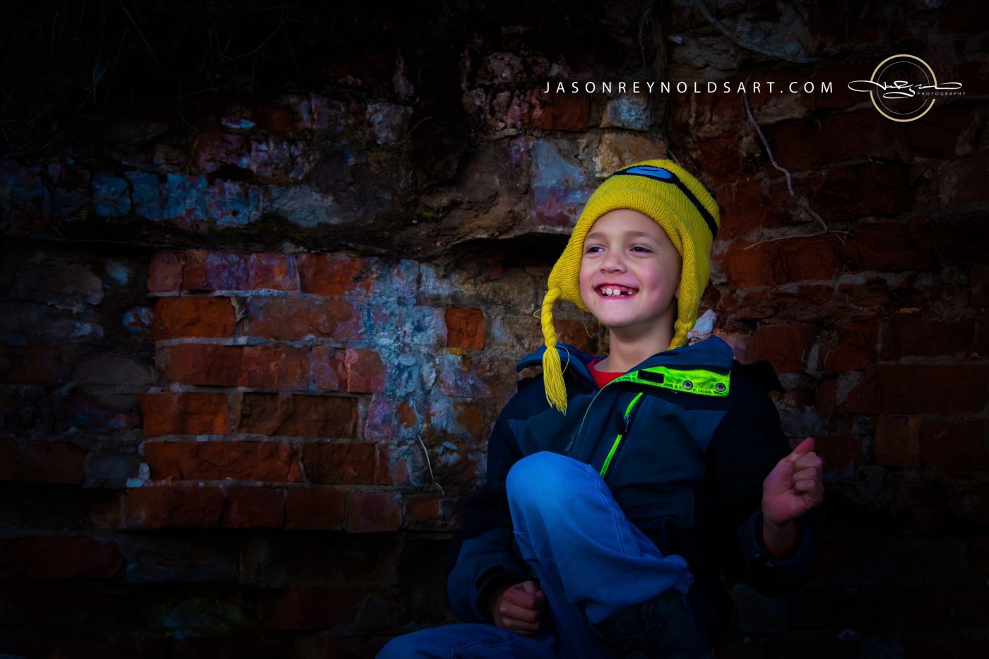 Boy in yellow knit hat against weathered brick wall