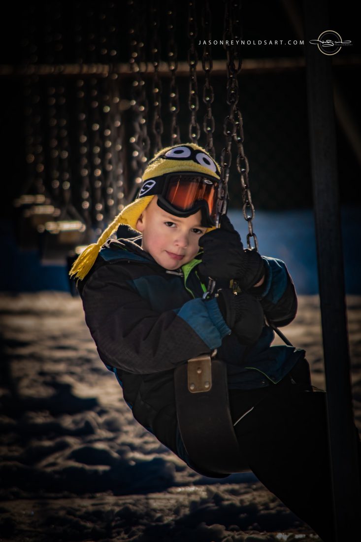 Child on Swing in Snow with Yellow Knit Hat