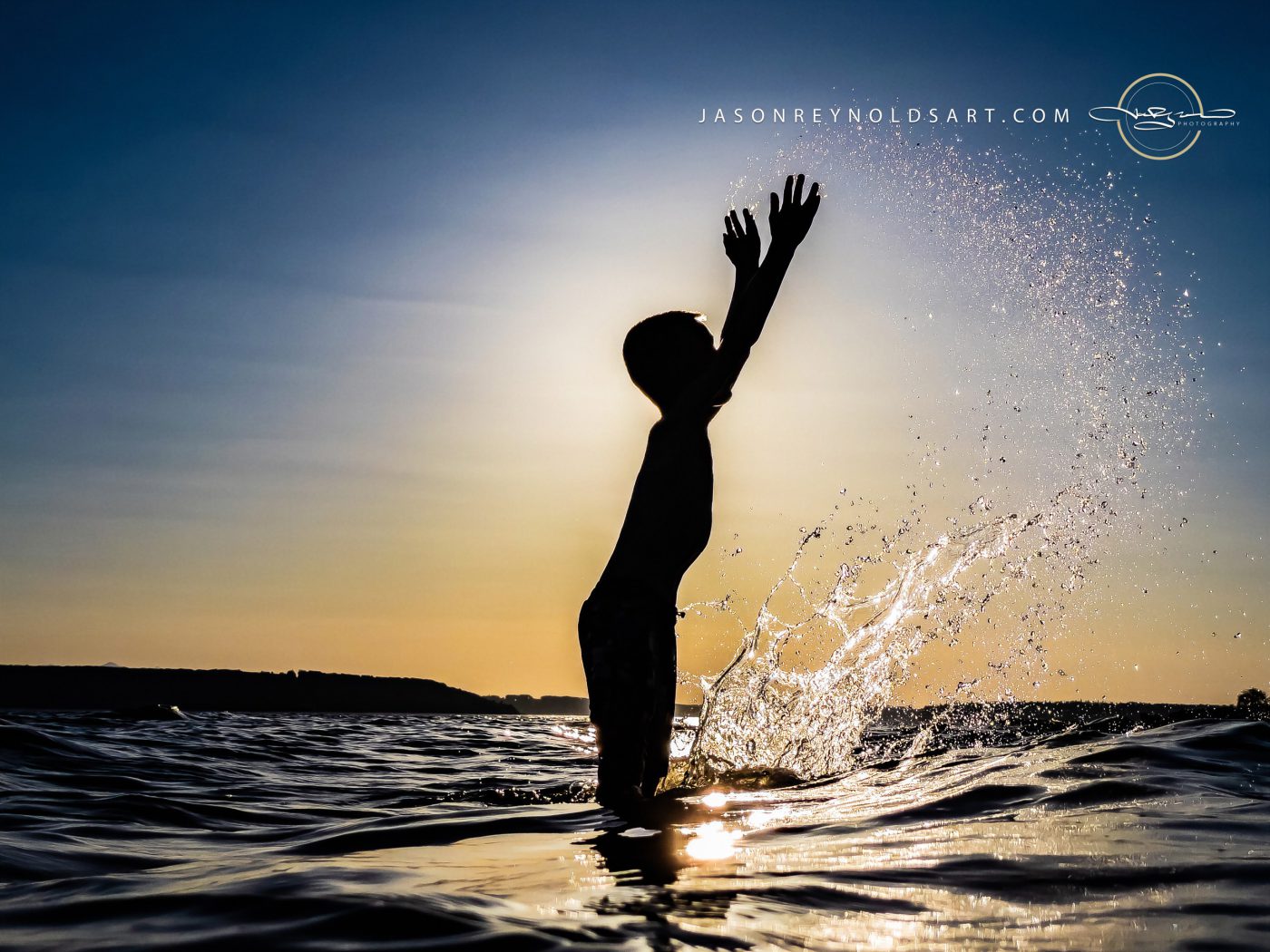 Child silhouetted tossing a spray of water at sunset