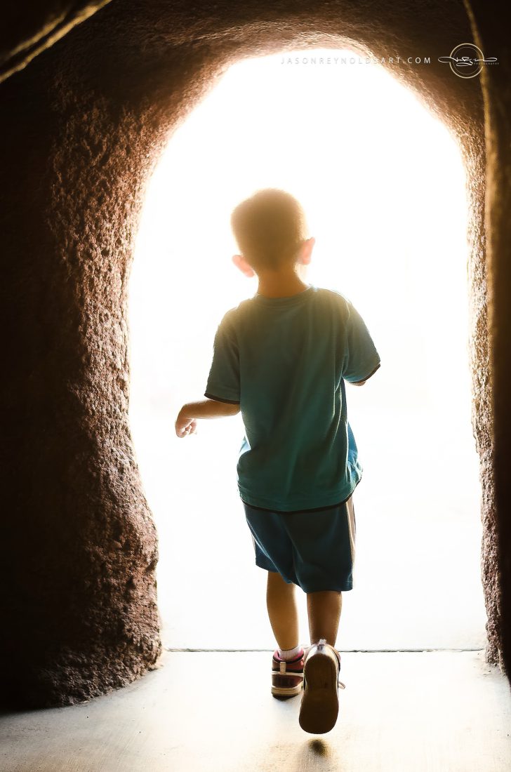 Child Walking Toward Bright Light Through Stone Arch