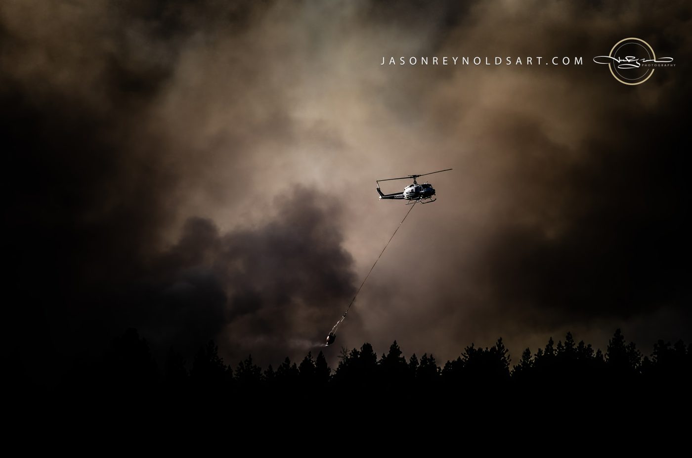 Helicopter Carrying Bambi Bucket Above Smoky Pine Silhouette