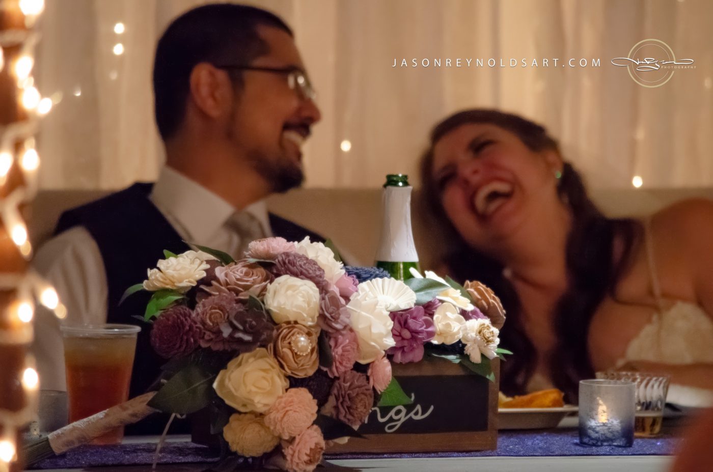 Laughing couple behind bridal bouquet and champagne bottle