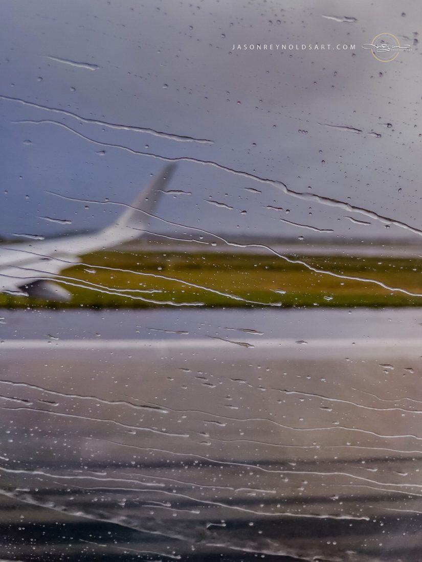 Raindrops on airplane window with blurred wing and runway