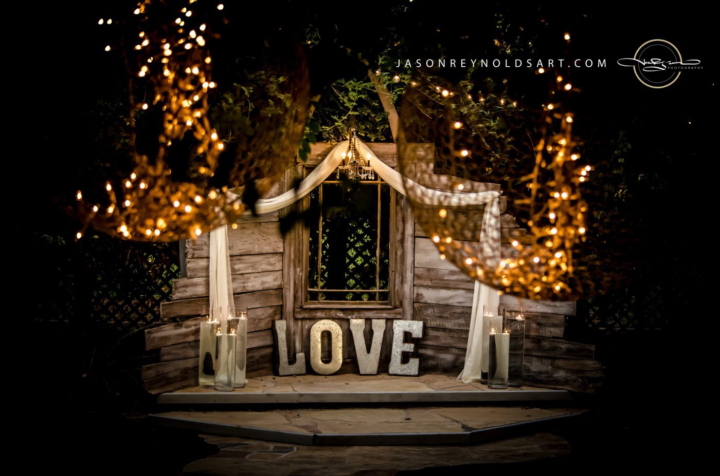 Rustic ceremony stage with large 'LOVE' letters and warm string lights