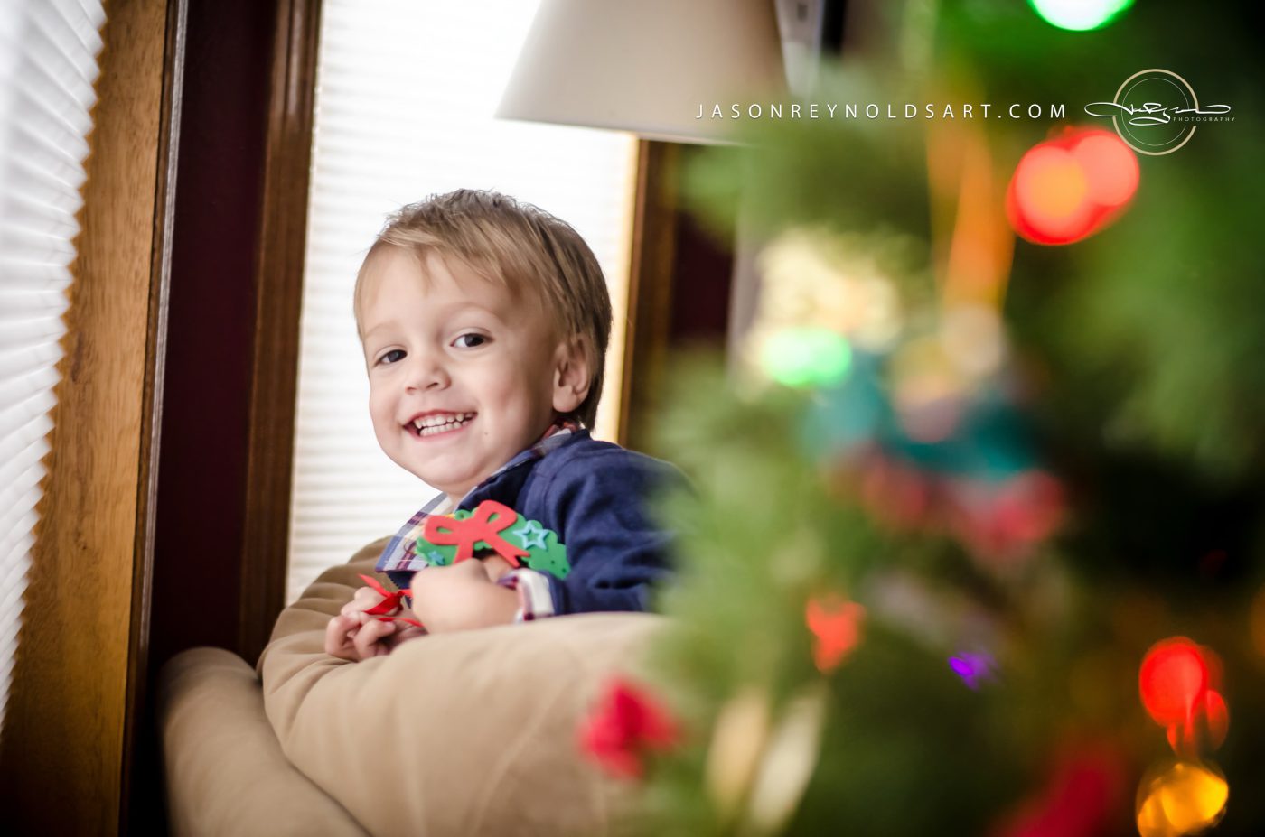 Smiling toddler on couch with decorated tree bokeh